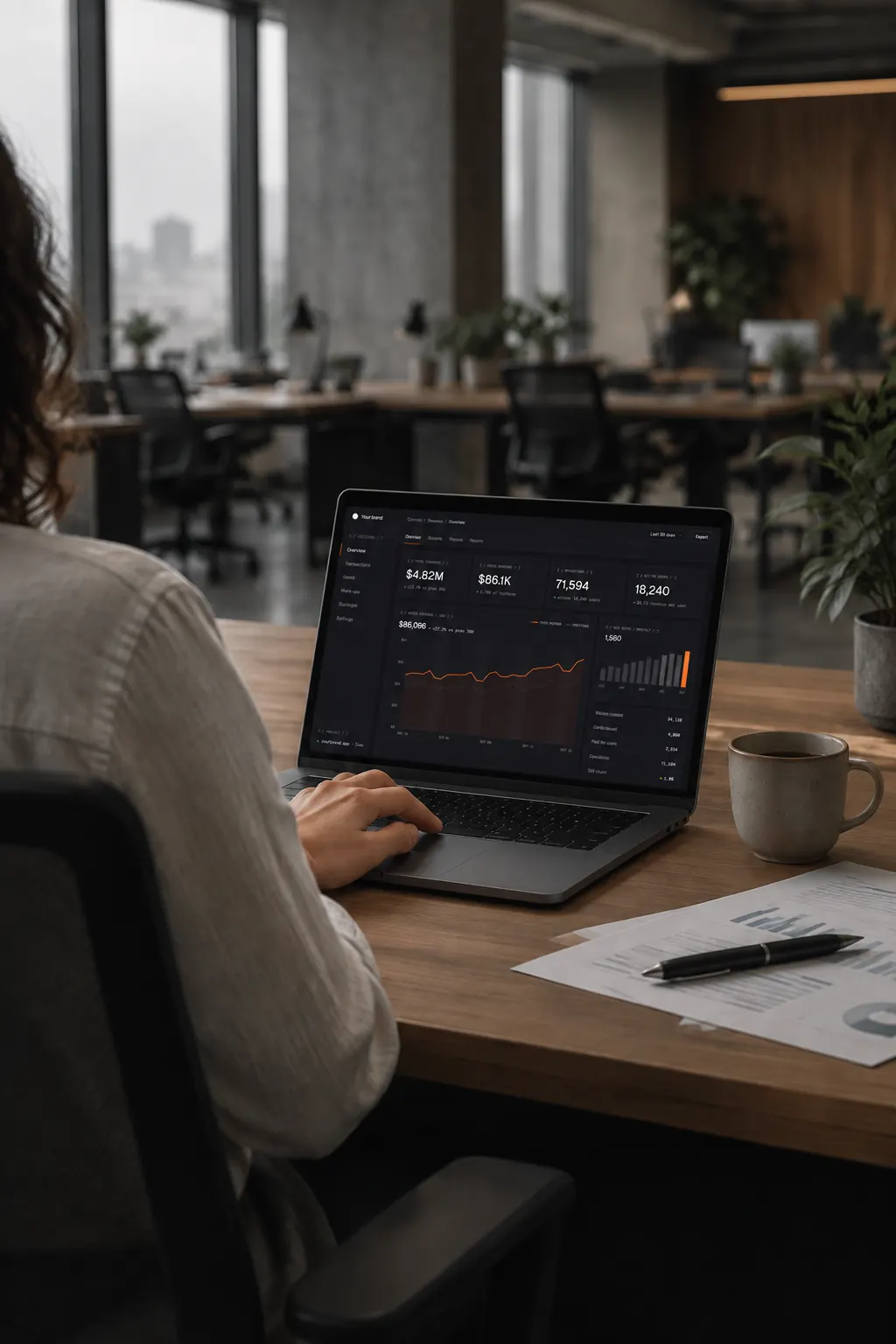 A person at a desk in an office, the Your brand admin console open on a laptop, showing revenue for the last 30 days.